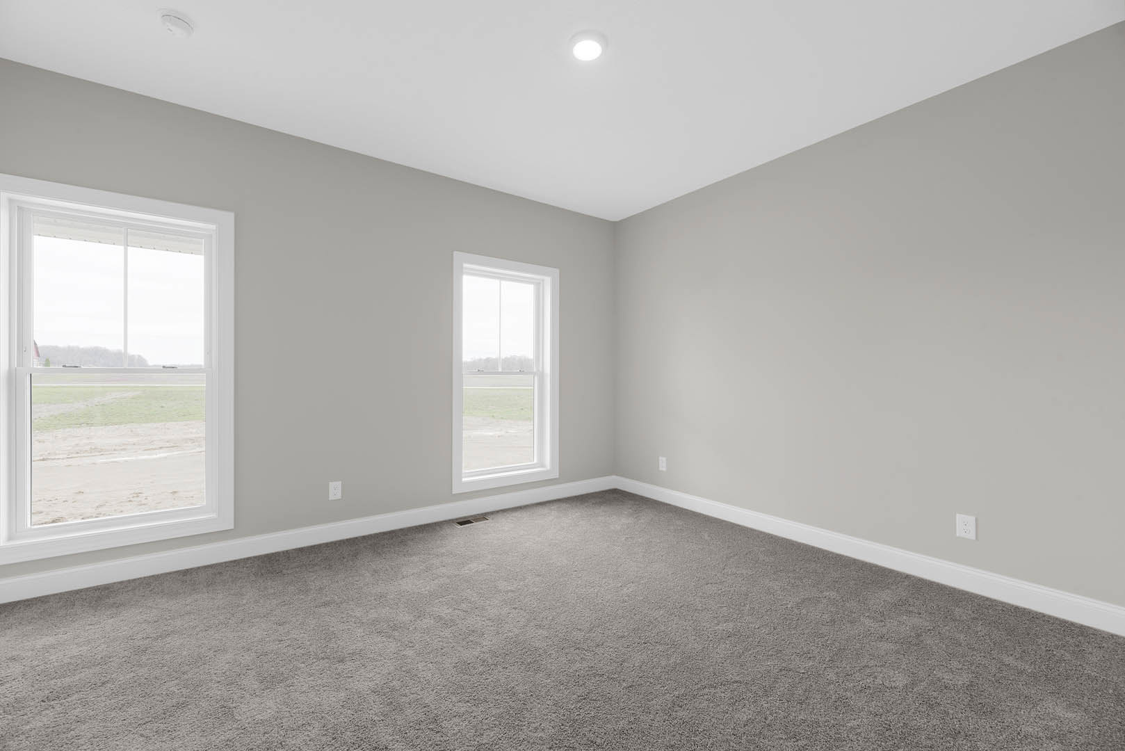 Room with grey carpet, white walls, large windows overlooking grassy field, recessed ceiling light, simple baseboard molding