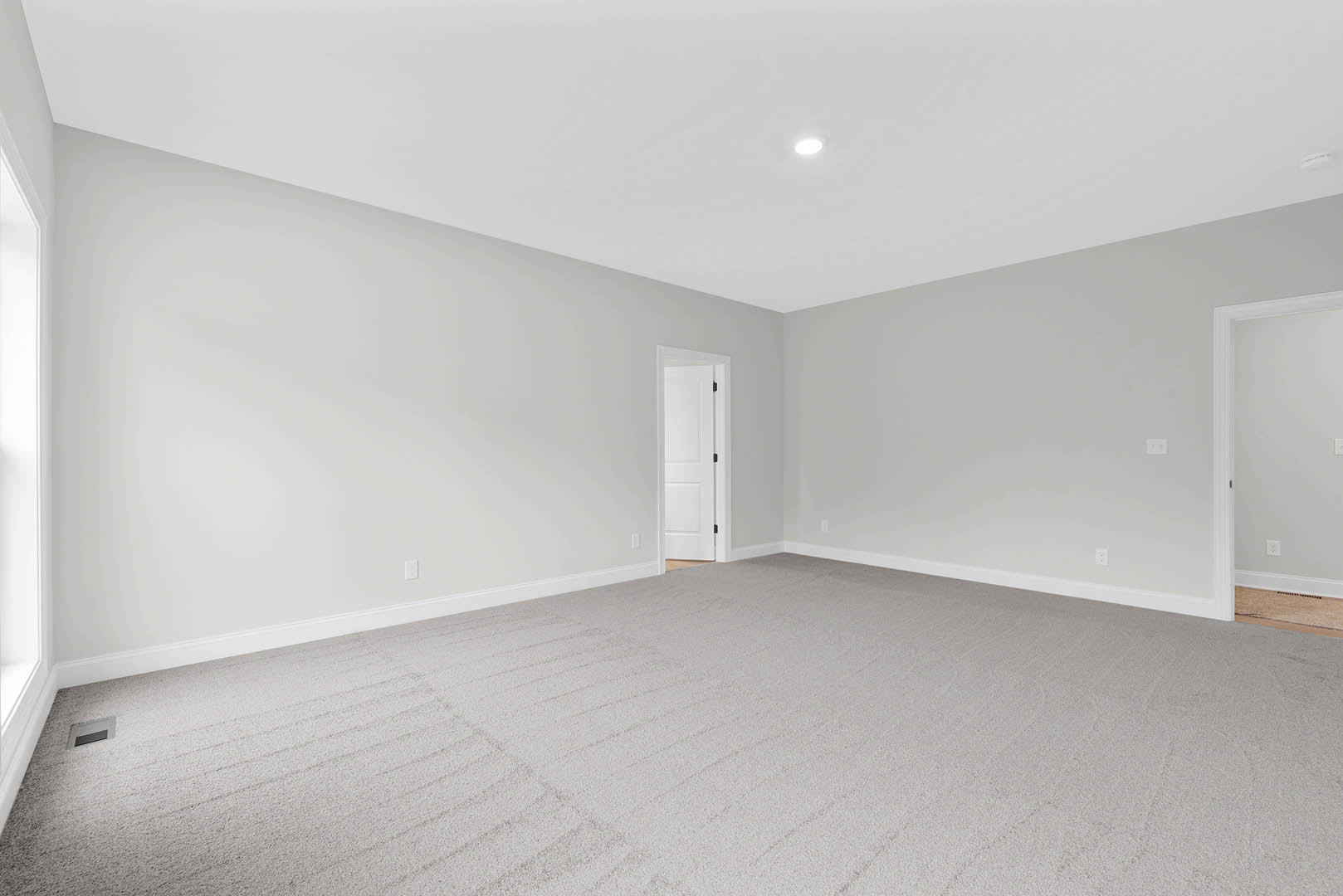 White paneled door with black hardware open to a room featuring white plaster walls, wood flooring, and a central ceiling light.