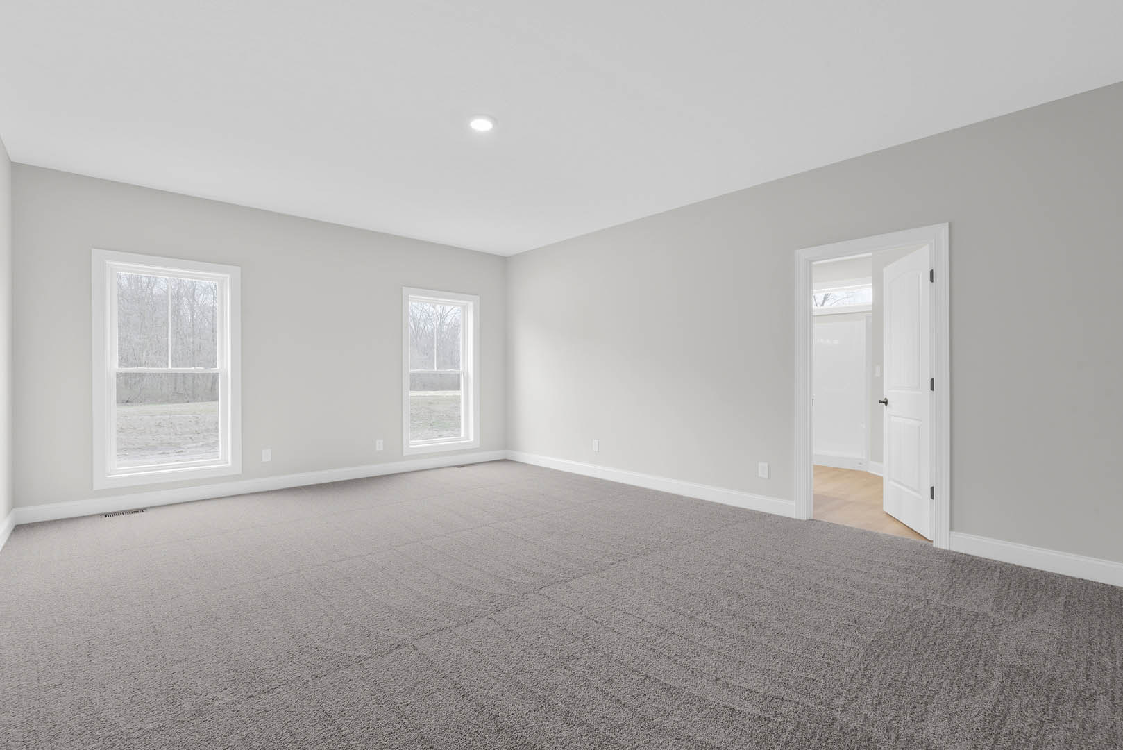 Carpeted bedroom with open white door, large windows overlooking snowy field and trees, neutral plaster walls