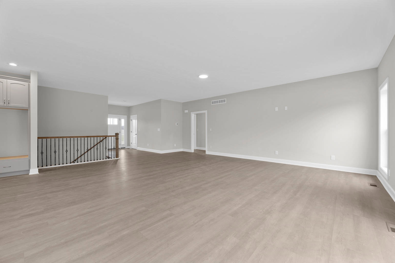 Spacious room with light wood flooring, white walls, and a staircase featuring a modern railing; recessed ceiling light and white door visible.