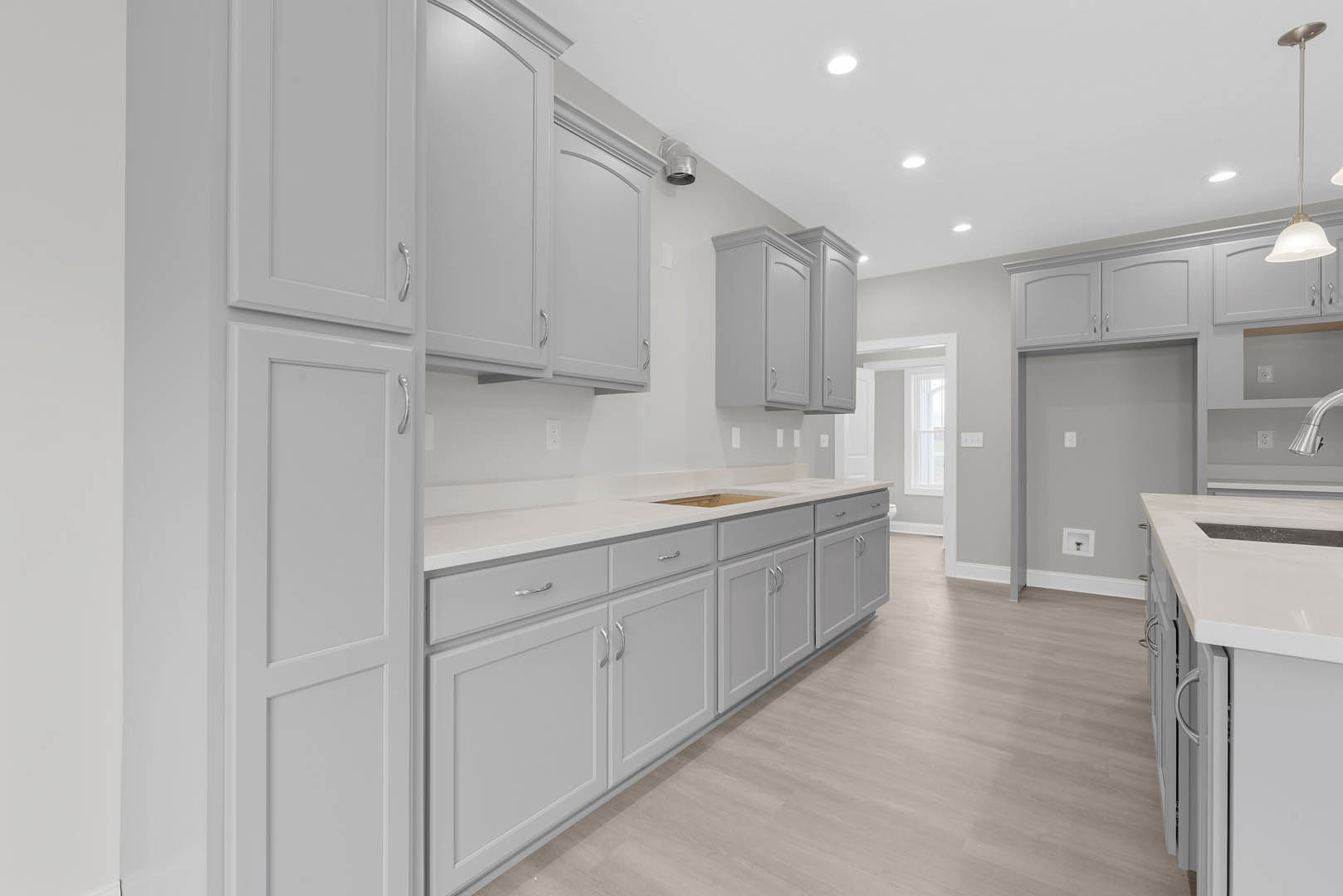 White kitchen cabinets with brushed metal handles, wood plank flooring, quartz countertop, stainless steel sink, and tiled backsplash.