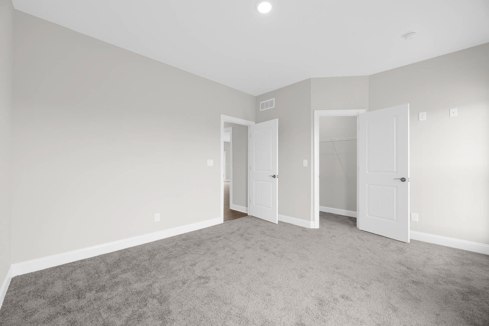 White-walled room with two white doors, one featuring a black handle and the other a silver handle, light gray carpet flooring, recessed ceiling lights, and smooth plaster