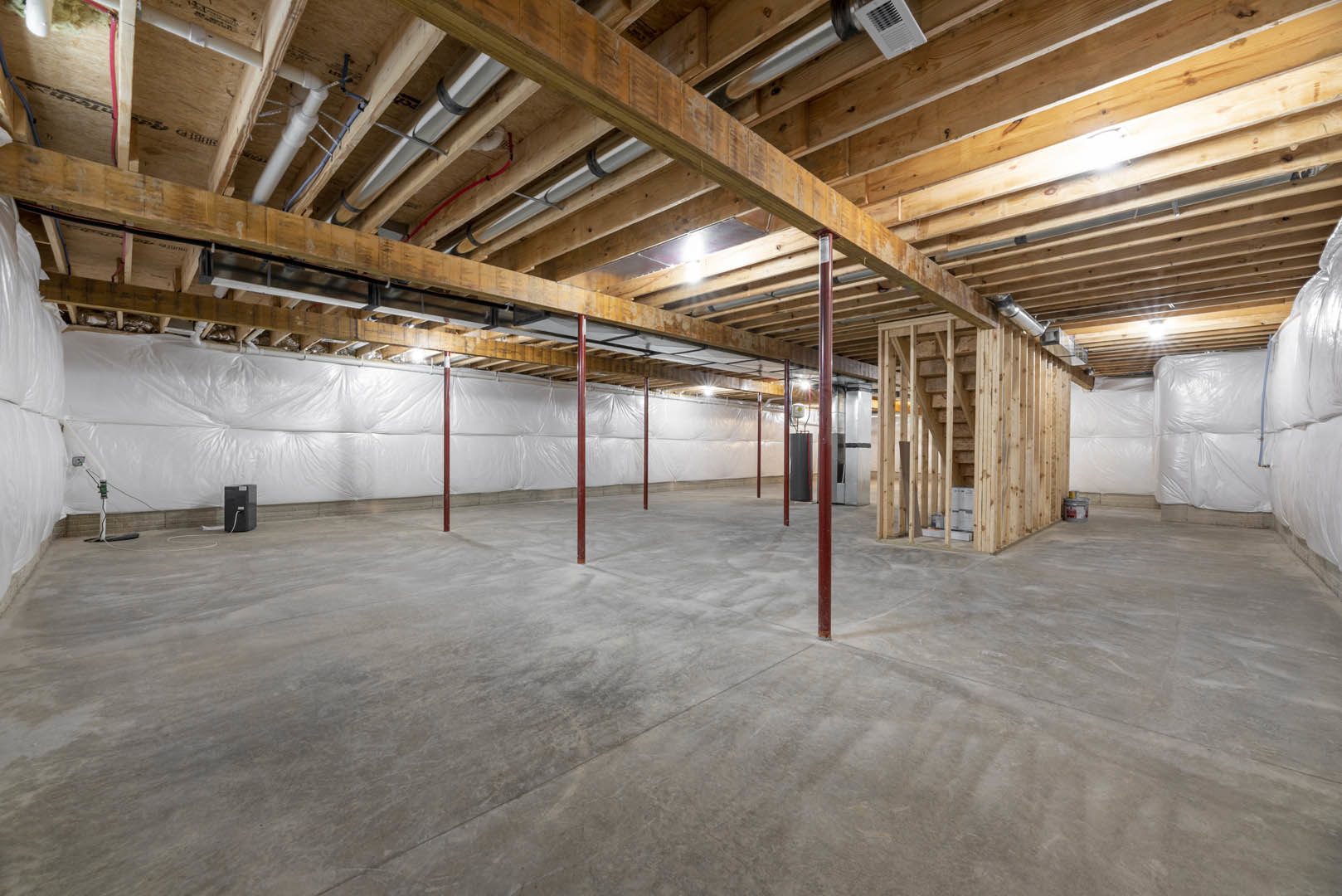 Exposed wood ceiling beams, white drywall, concrete floor with red support poles, visible ductwork and vent in unfinished basement space