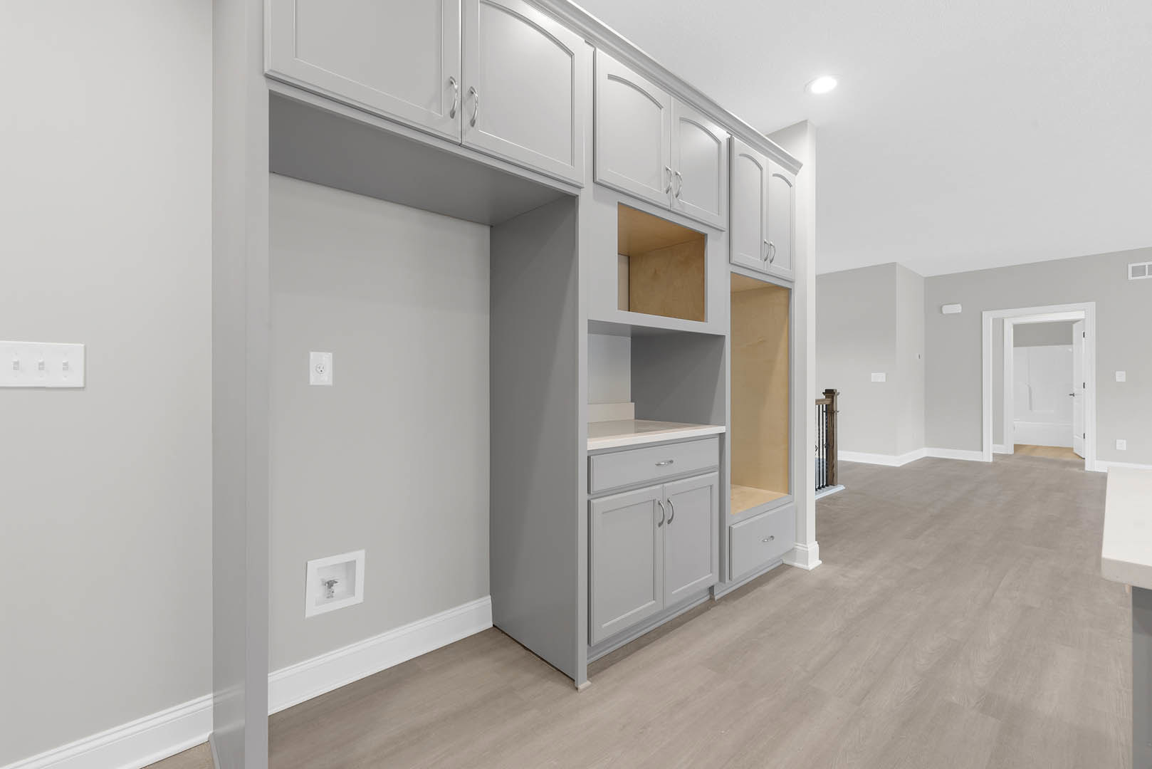 White built-in cabinets and open shelving against a light wall, with a white door ajar, wood flooring, and a wall outlet visible.