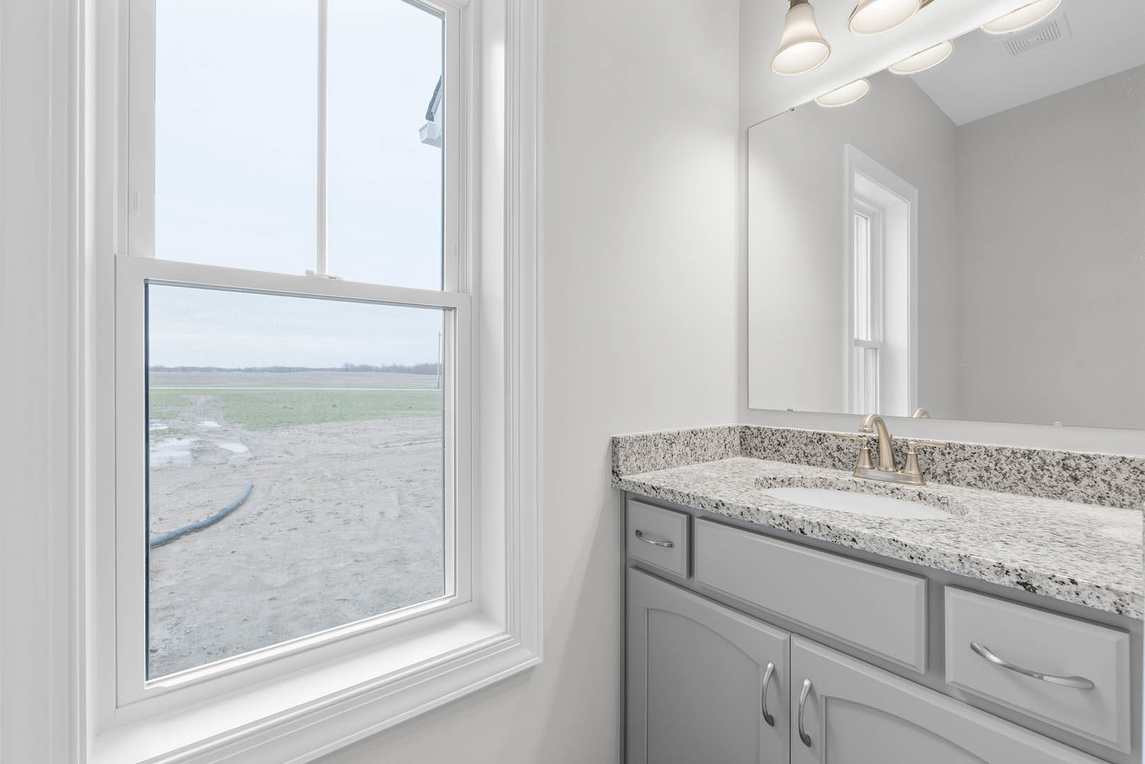 Bathroom with a large white-framed window overlooking a field, modern sink with chrome faucet, light-colored countertop, and cabinetry with drawers.