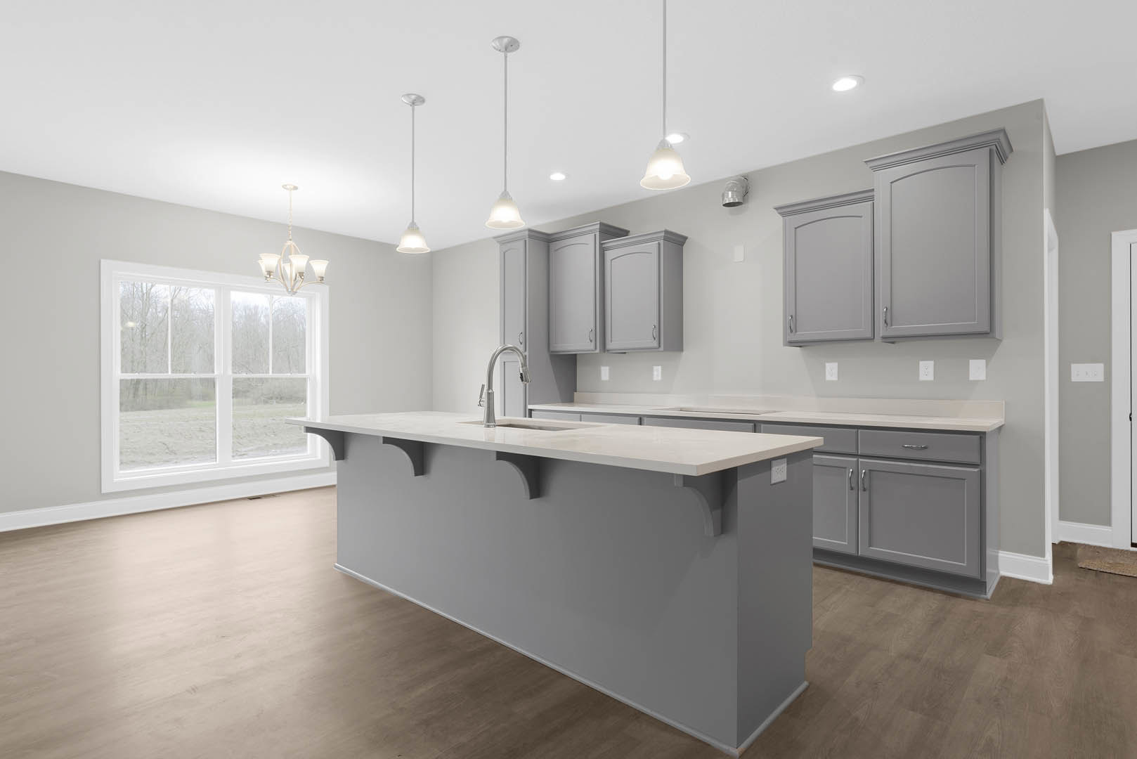 Spacious kitchen featuring a large island with white countertop and built-in sink, wide window overlooking outdoors, white cabinetry with curved tops, and a white door with arched
