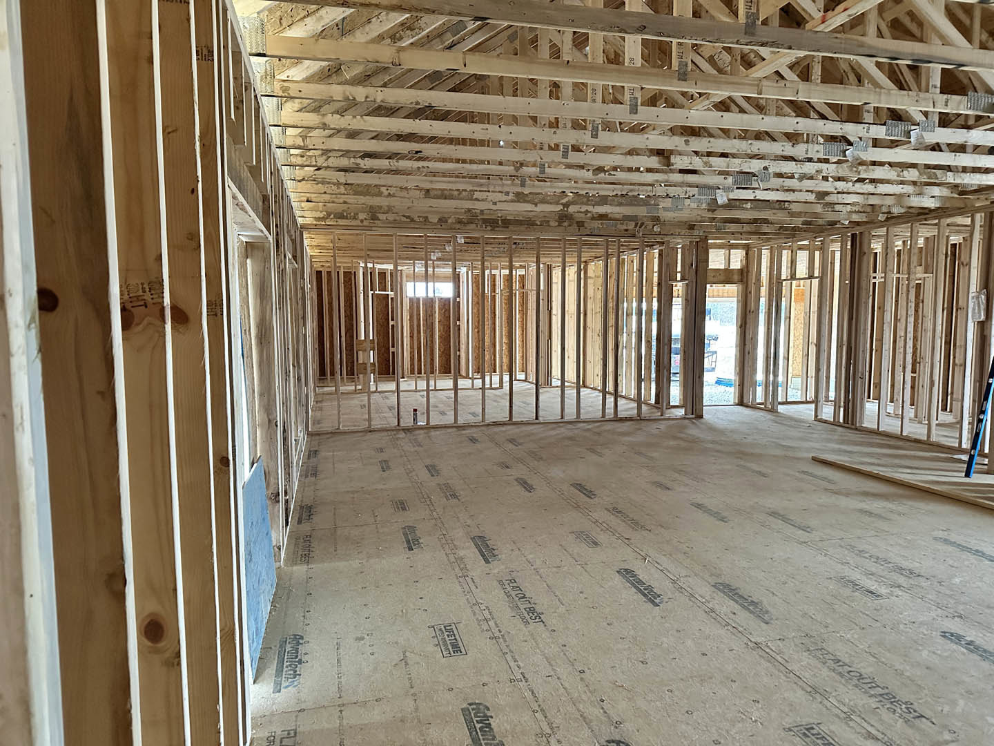 Living room with exposed wood ceiling beams, large window, blue accent wall, and light-colored plank flooring.
