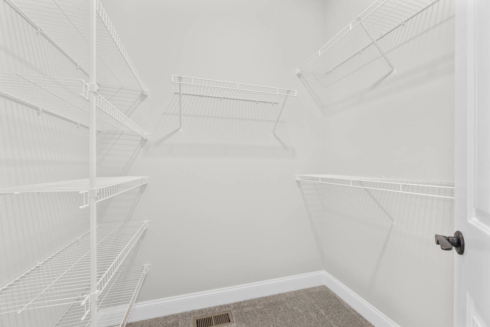 White built-in shelves against a plaster wall, metal hanging bar, carpeted floor, and close-up of a door handle in a residential interior.