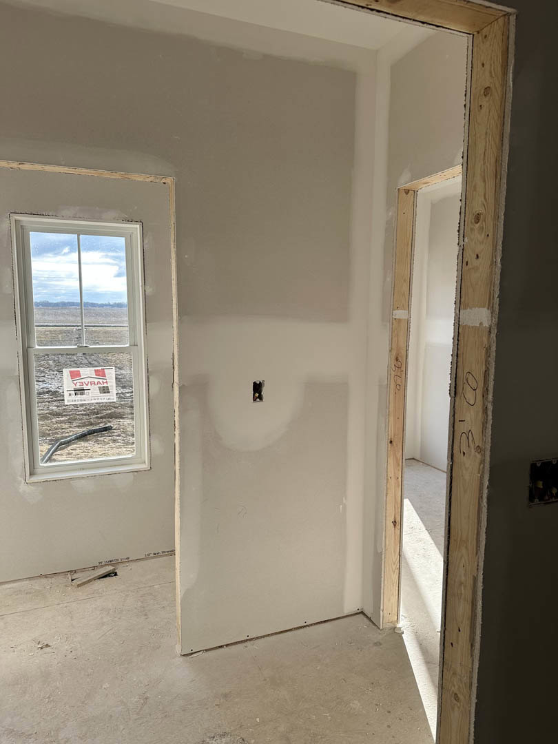 White plaster walls with a rectangular window featuring a sign, adjacent to a closed door; smooth flooring with a dark cable or hose lying near the baseboard.