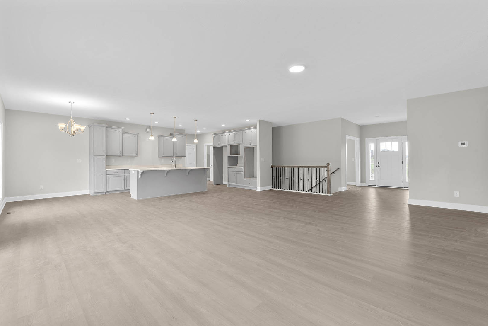 Spacious open-plan room featuring wood laminate flooring, modern kitchen with white cabinetry, glass-paneled door, staircase with metal railing, white shelving, and a contemporary