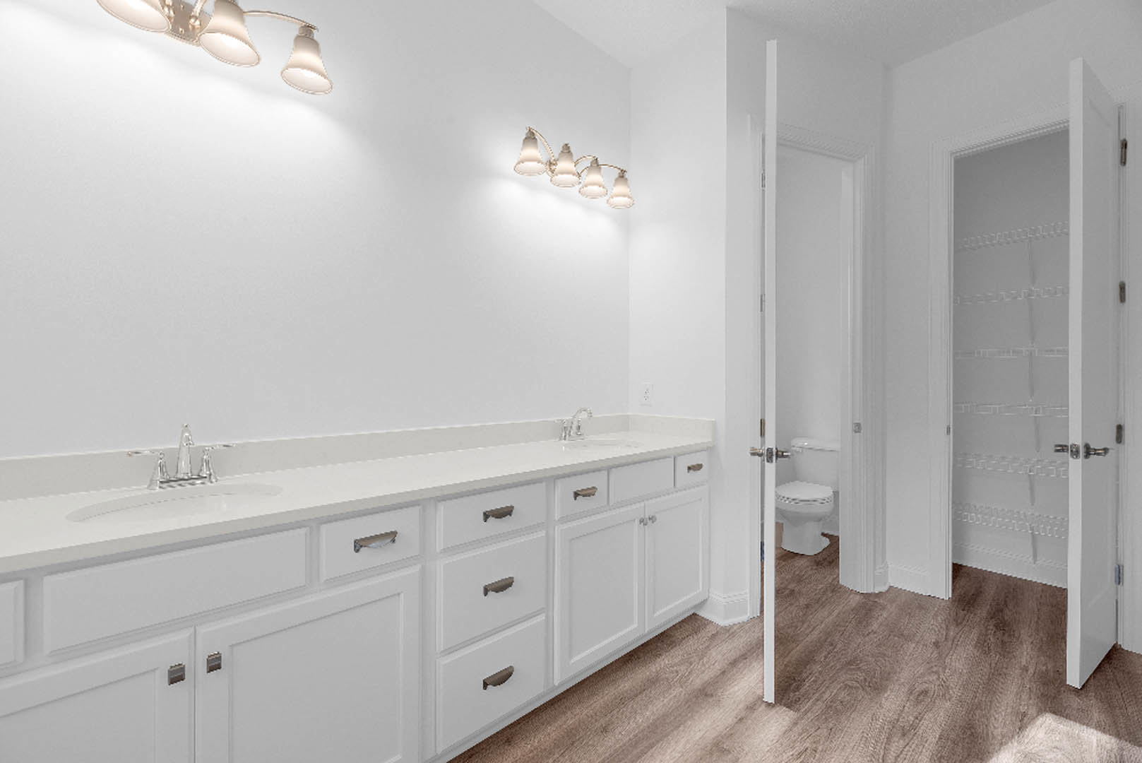 Bathroom with white shaker cabinets, wood plank flooring, white countertop and sink, chrome faucet, modern light fixture, and white toilet