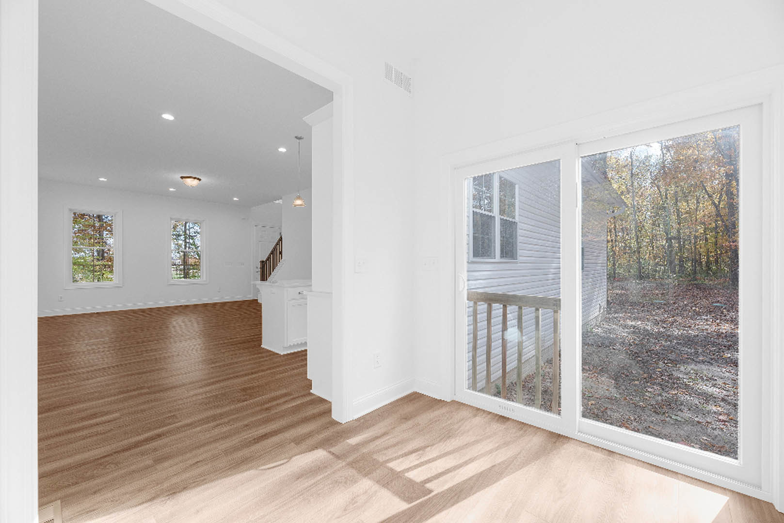 Sliding glass door with white frame opening onto view of trees and neighboring house, wooden laminate flooring, plaster walls.