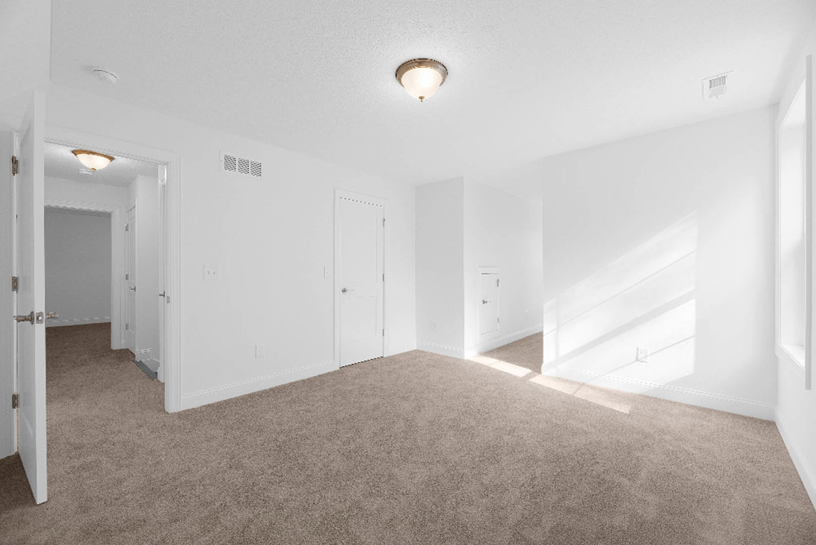 Carpeted room with white walls, ceiling vent, modern light fixture, and white door with silver handle
