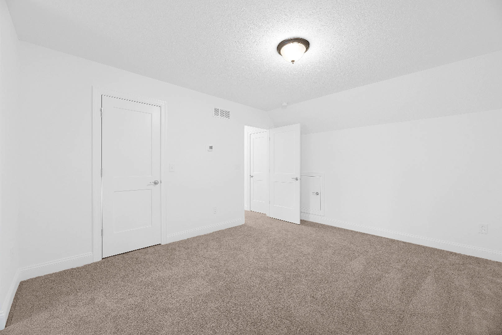 Carpeted room with white plaster walls, white doors featuring silver handles, and a close-up of a modern light fixture on the ceiling