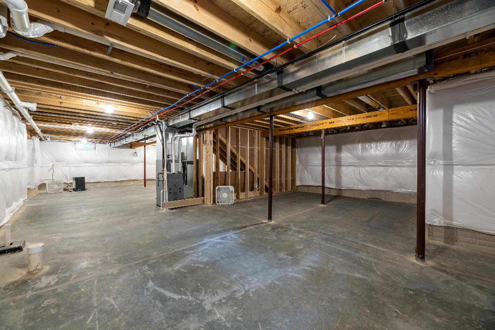 Concrete floor with exposed steel beam, visible ceiling pipes, white vent, and industrial fan in unfinished basement interior