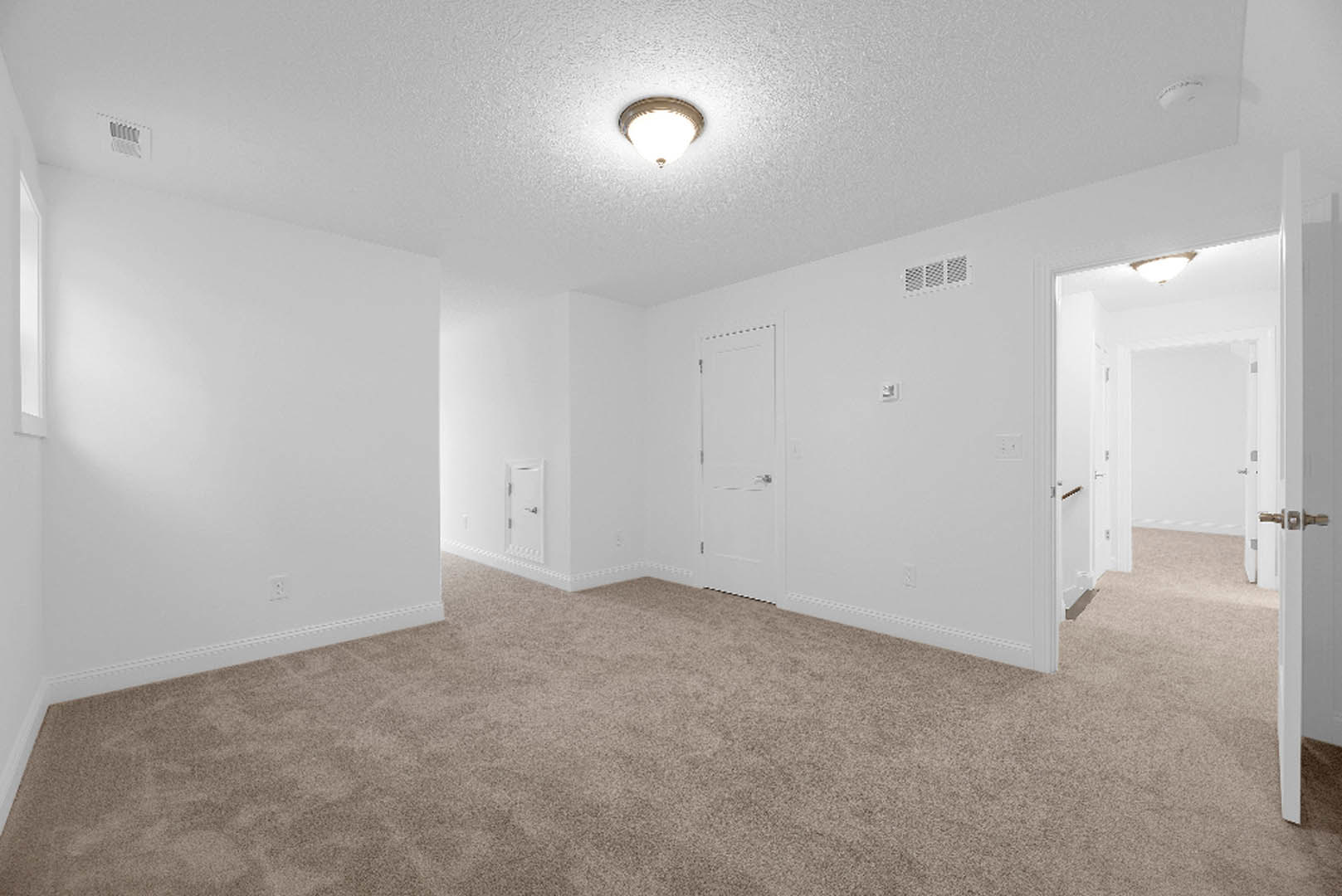Carpeted room with white walls, white door with silver handle, ceiling light fixture, and floor vent