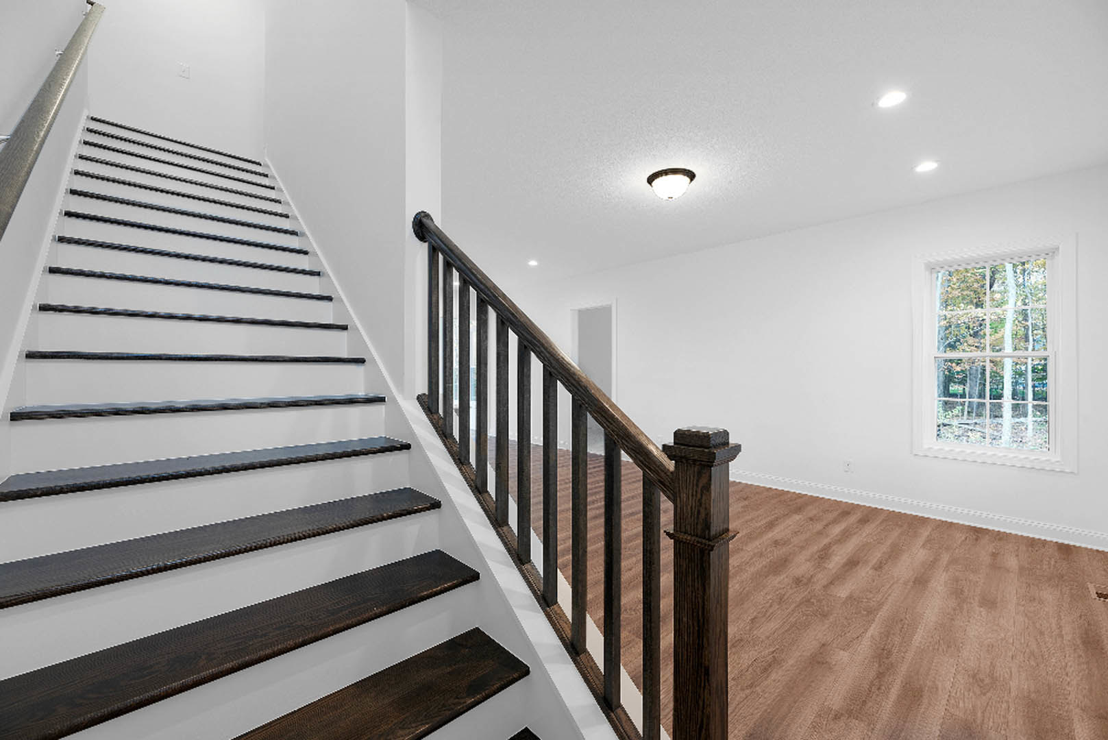 Wooden staircase with matching handrail and balusters, plaster walls, large window overlooking trees, ceiling-mounted light fixture, close-up of pillar and stair treads