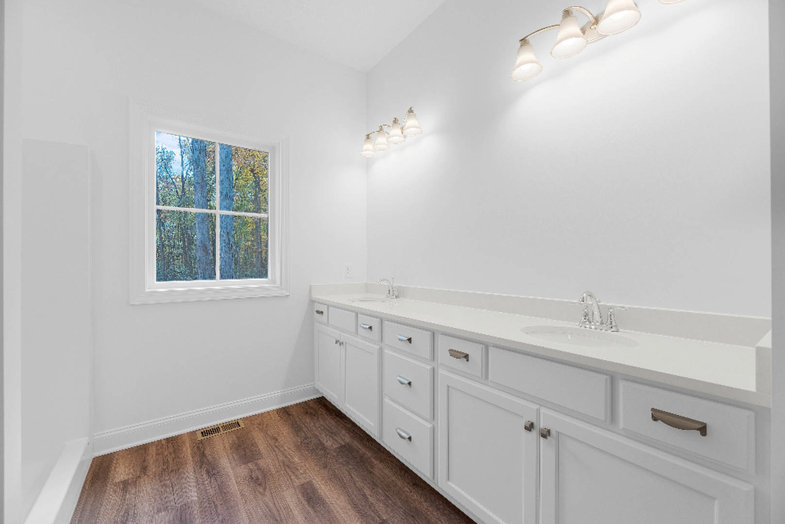 White bathroom cabinets beneath a wide window with outdoor trees visible, chrome faucet and sink, light fixture overhead, tiled floor and walls, vent near ceiling.