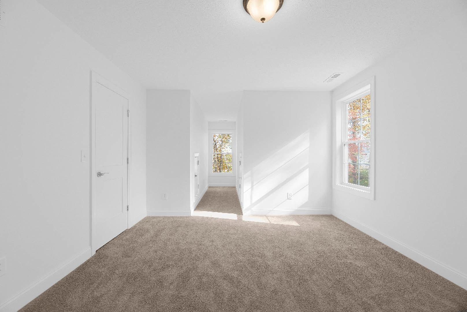 White carpeted floor, white walls, window with white frame, ceiling fixture, white door with silver handle, natural light streaming through