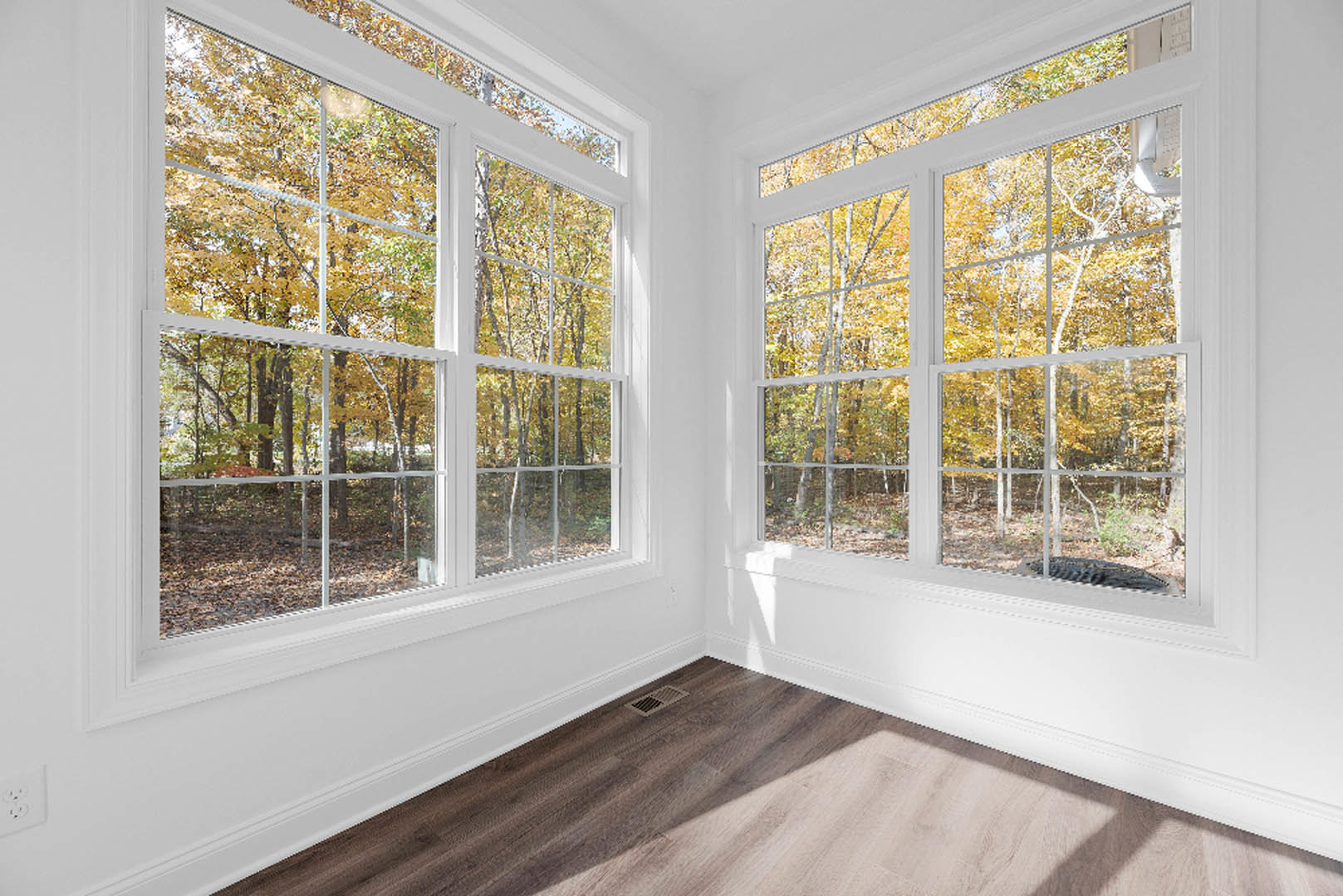 Spacious room featuring multiple large windows with views of trees, wood flooring with a vent, white ceiling with skylight, and a bathtub drain visible; white surfaces accented