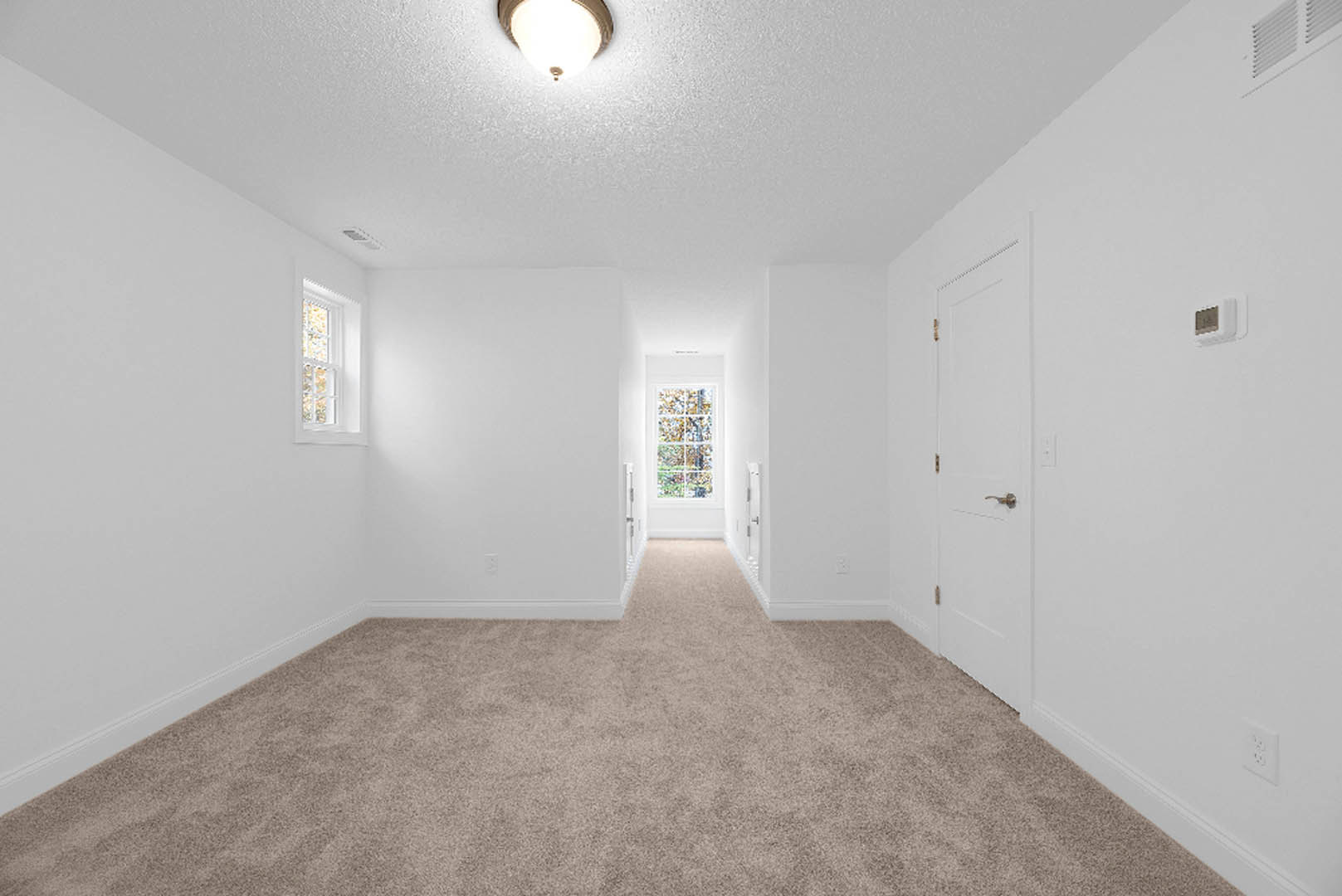 Neutral-toned carpeted room with white walls, ceiling-mounted light fixture, and window with white frame letting sunlight onto the floor