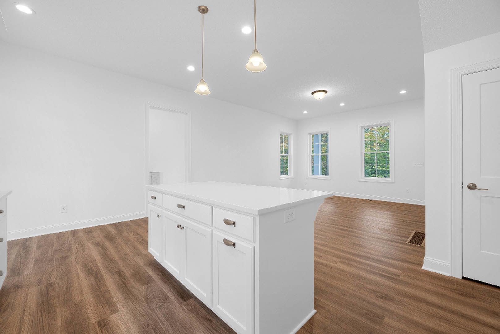 White kitchen with wood flooring, central island featuring drawers, white cabinetry, window overlooking trees, cluster of pendant lights, close-up details of door handle and window