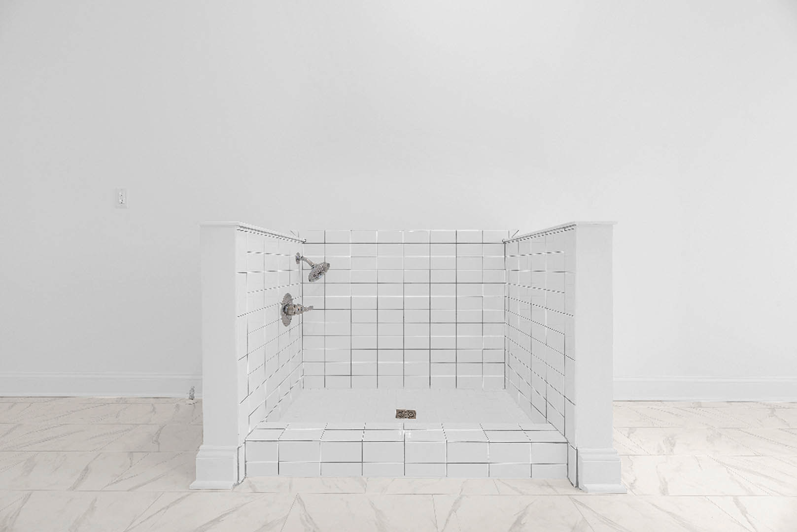Shower with white tile walls, white tile floor and central drain, chrome shower head mounted on tile wall
