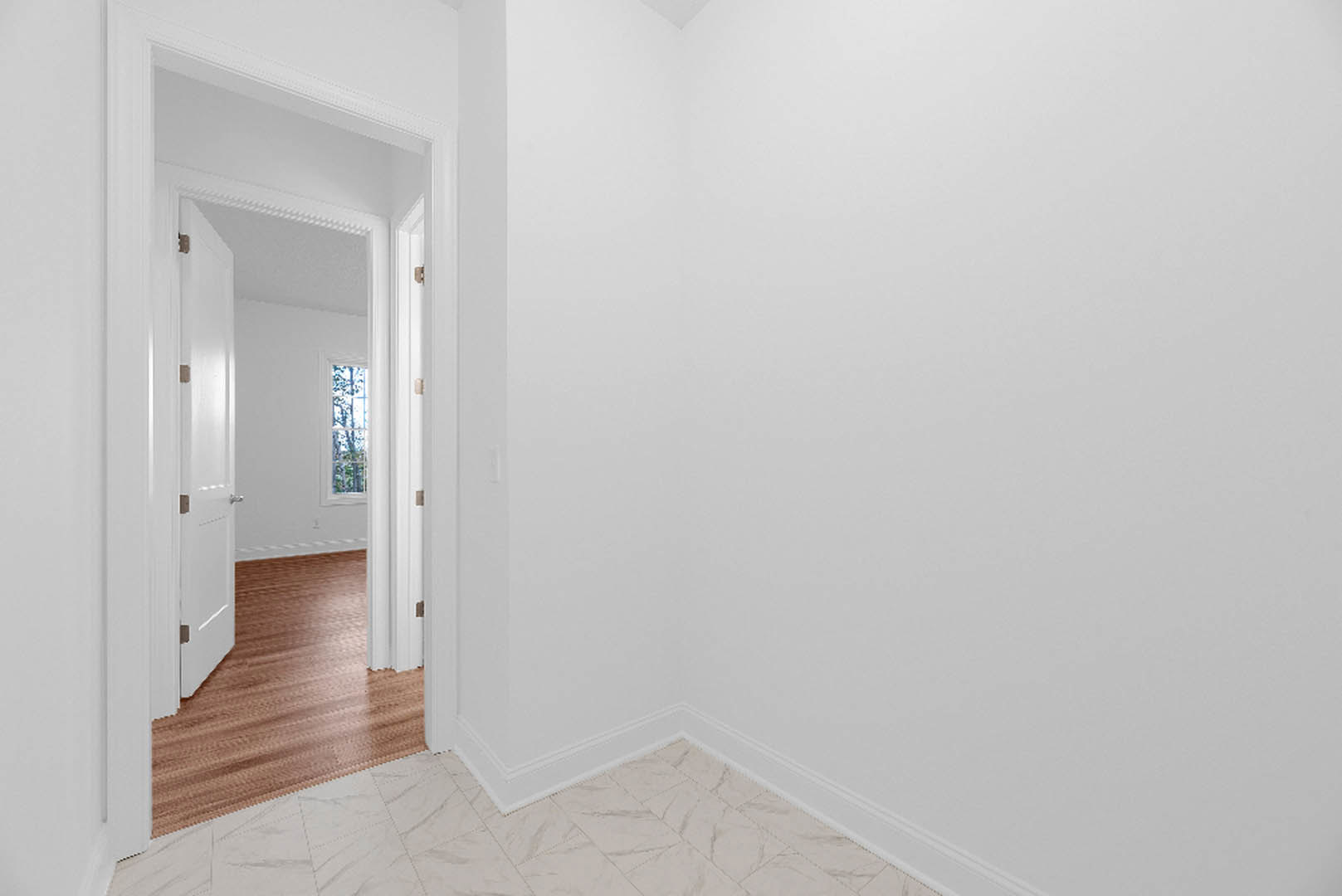 White-walled room with polished marble floor, large window overlooking trees, and white doors