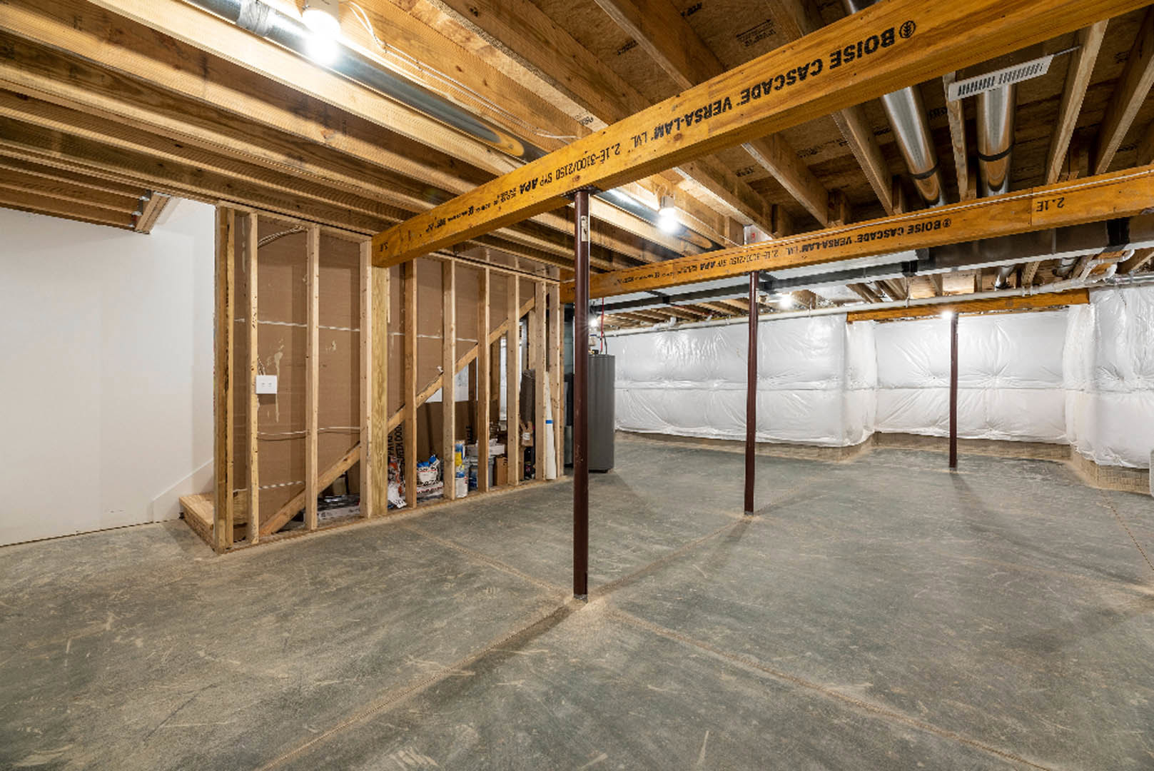 Exposed wooden ceiling beam, white plastic wall covering, concrete floor with metal support pole, vent detail, and white wall corner in unfinished interior space