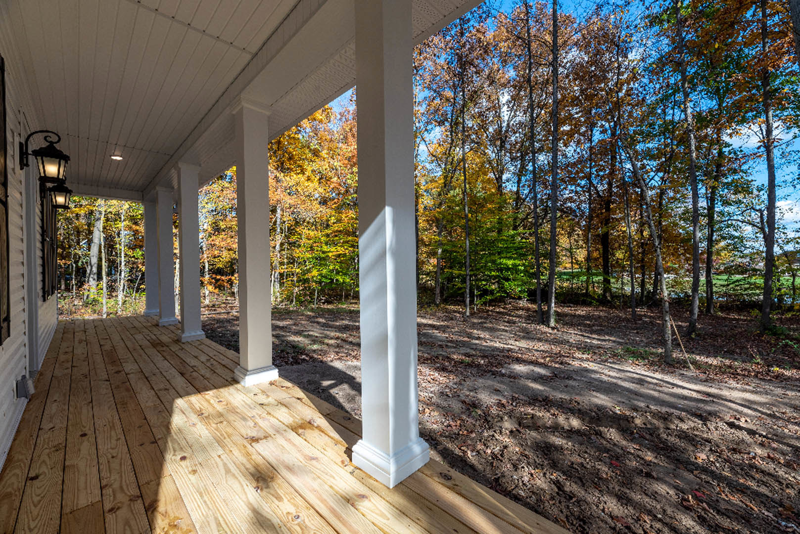 Covered porch with white pillars, wood decking, and leafy trees in the background