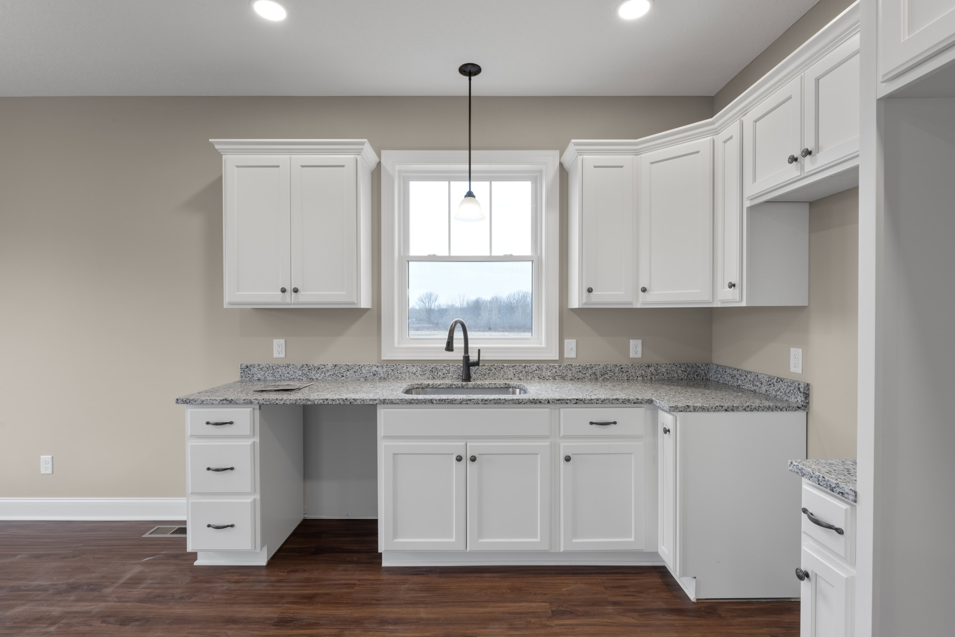 White kitchen cabinets with black hardware, black undermount sink, granite countertops, stainless steel faucet, and recessed lighting.