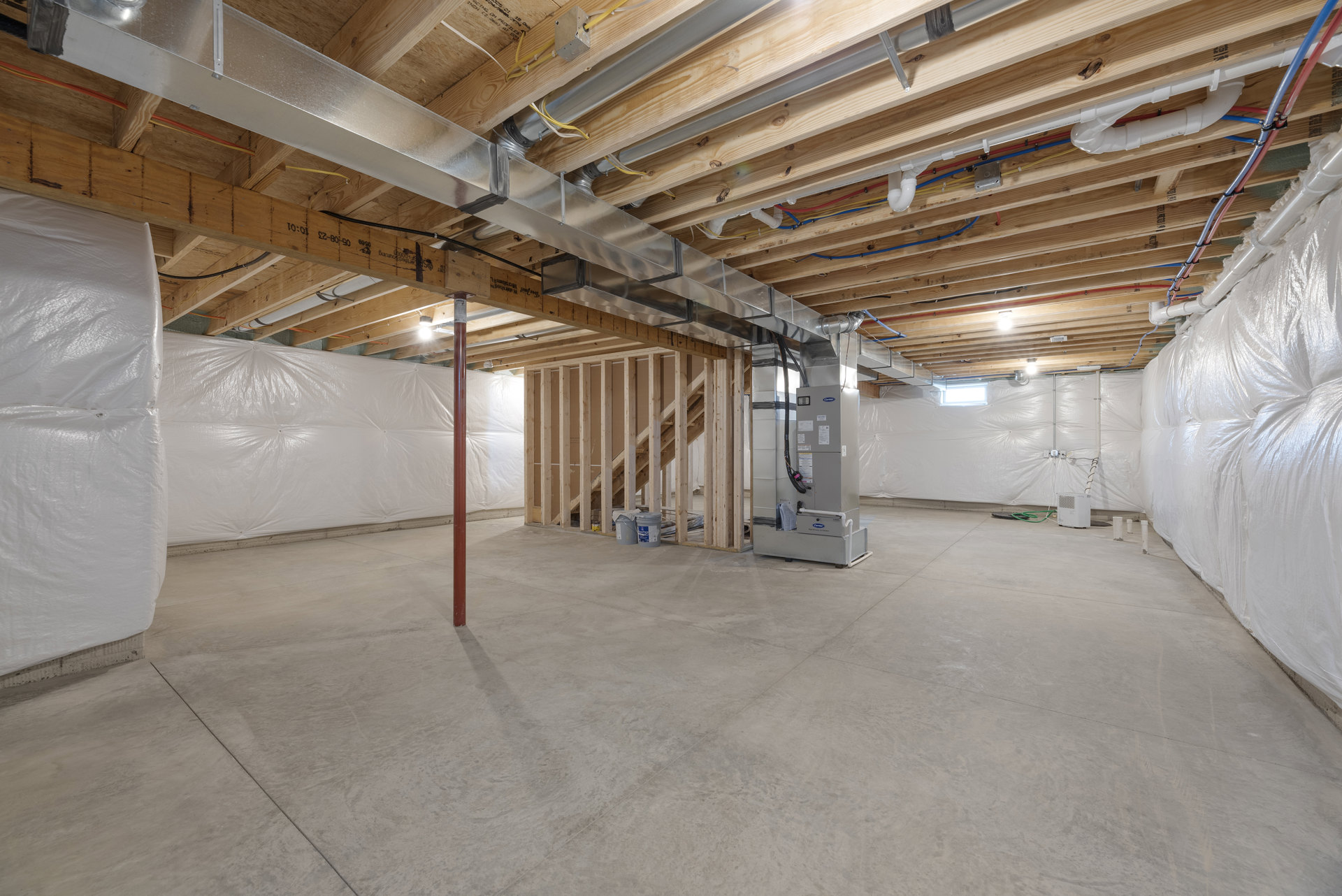 Living room with exposed wood beams and ceiling, plaster walls, concrete floor, and construction materials including buckets, pipes, and wiring.