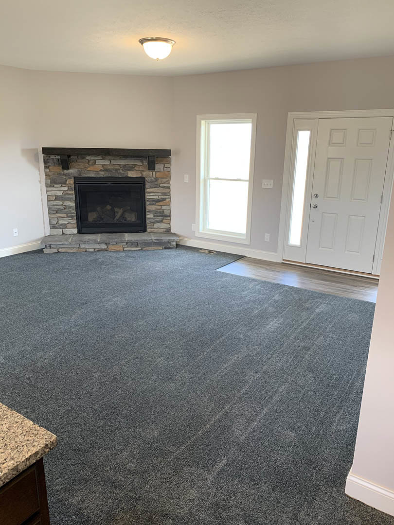 Living room with white walls, black-framed glass fireplace, white door letting in natural light, white-framed window, and carpeted floor