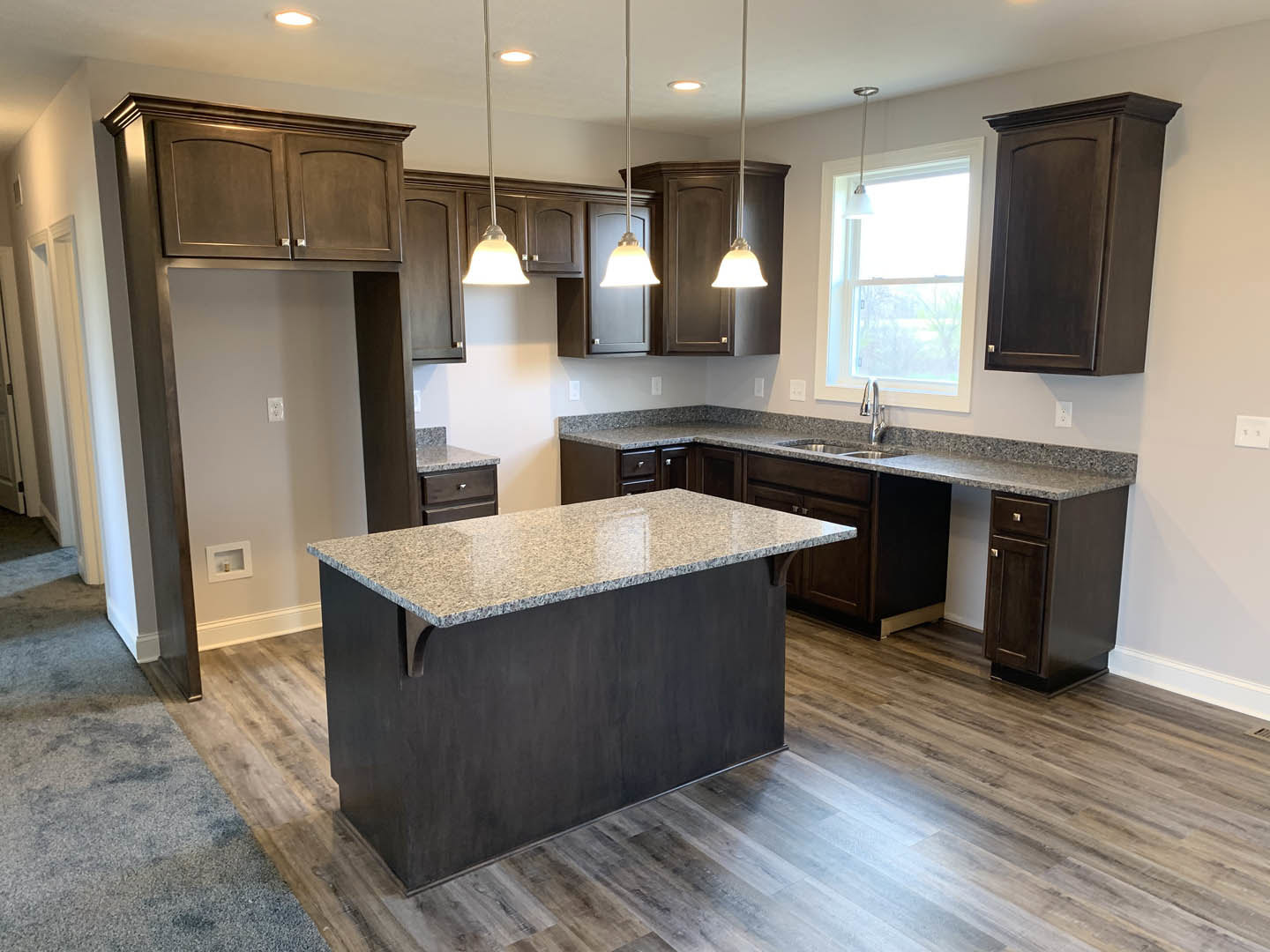 Kitchen featuring dark wood cabinetry, marble-topped island, black countertop, white cabinet door, tile flooring, window with natural light, and small bottle on windowsill