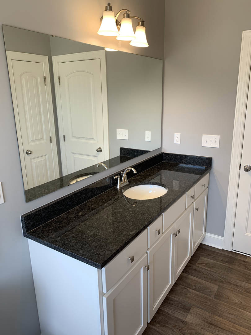 Bathroom with black granite countertop, rectangular mirror above sink, modern faucet, wood cabinetry, and tile flooring
