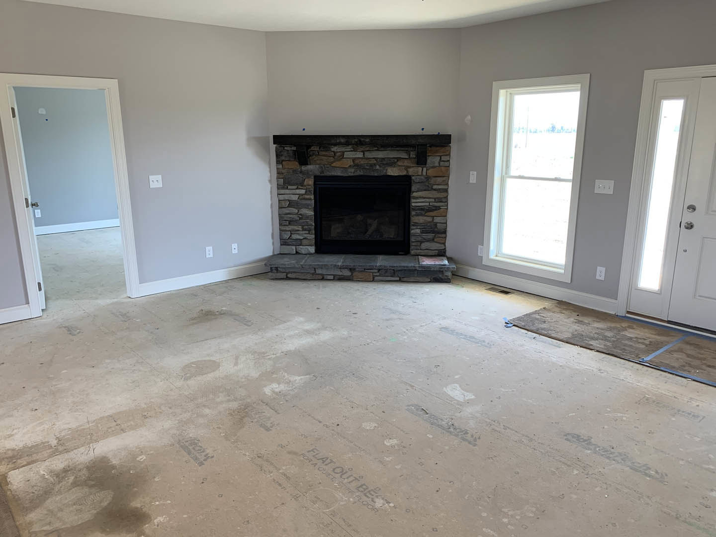 Living room with black-framed glass fireplace, white-framed window, light wood flooring, and white door illuminated by natural light
