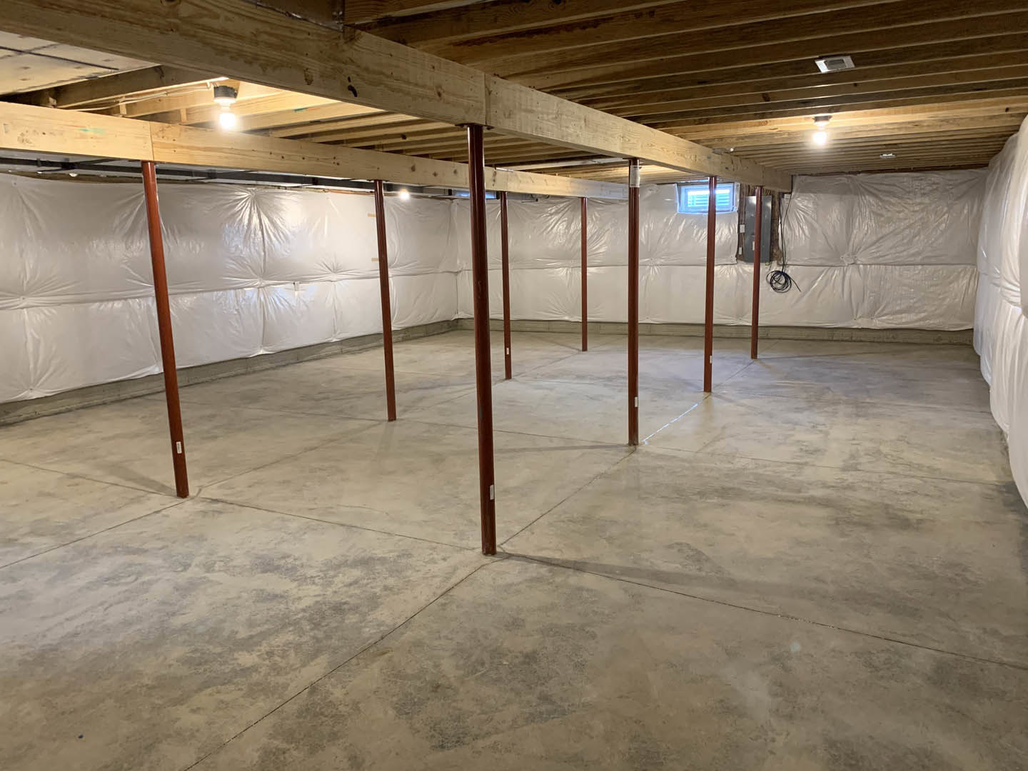 Basement with white painted walls, exposed wooden ceiling beams, concrete floor, and red support poles