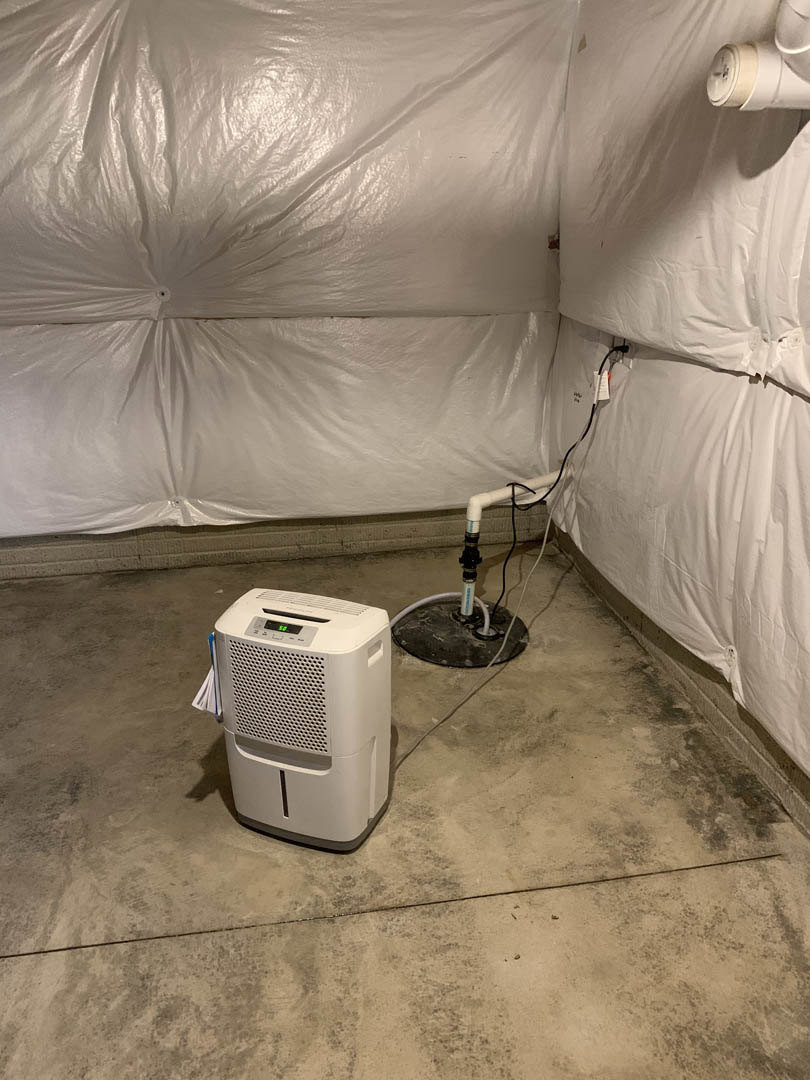 White rectangular home appliance with digital display and green indicator, positioned on light-colored flooring near a wall, with visible white pipes and plastic covering in a