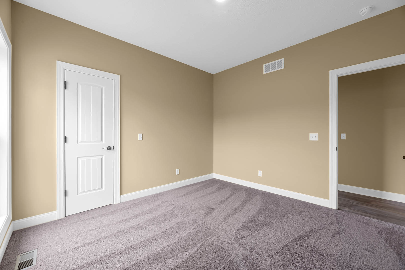 Beige walls with white doors featuring black handles, carpeted floor with a wall and floor vent, white ceiling and baseboard molding