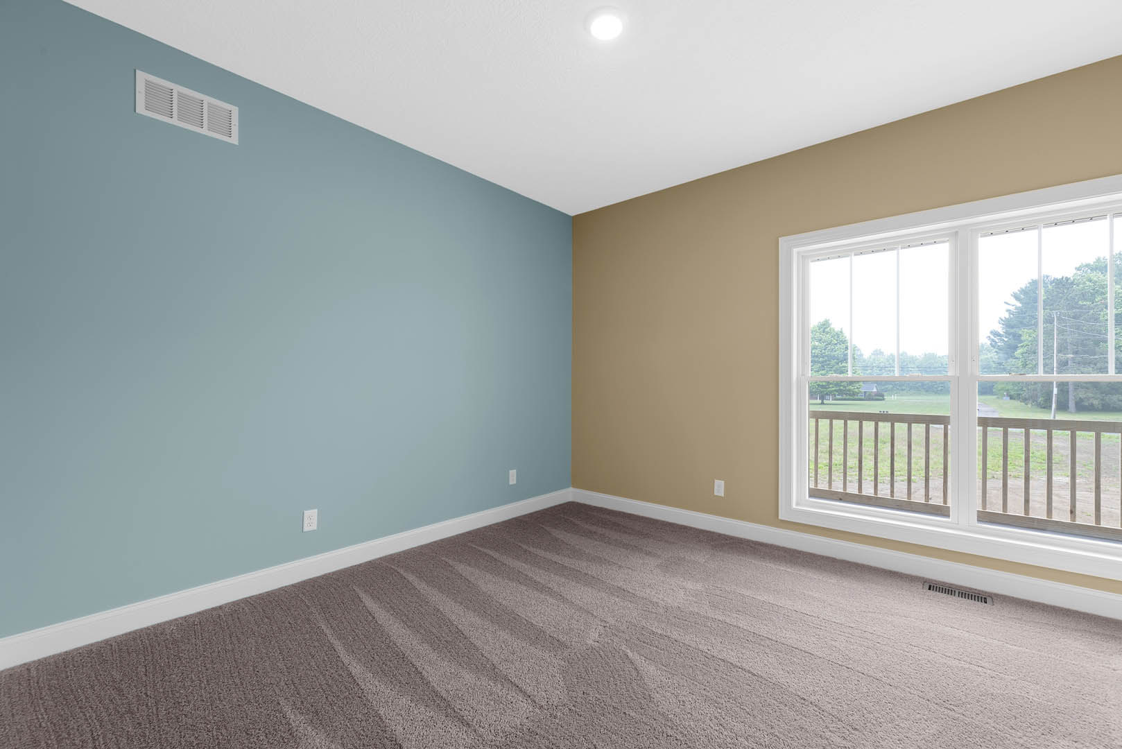 White-walled room with plush carpet flooring, large window overlooking a field and trees, glass door opening to balcony, ceiling vent, and crown molding