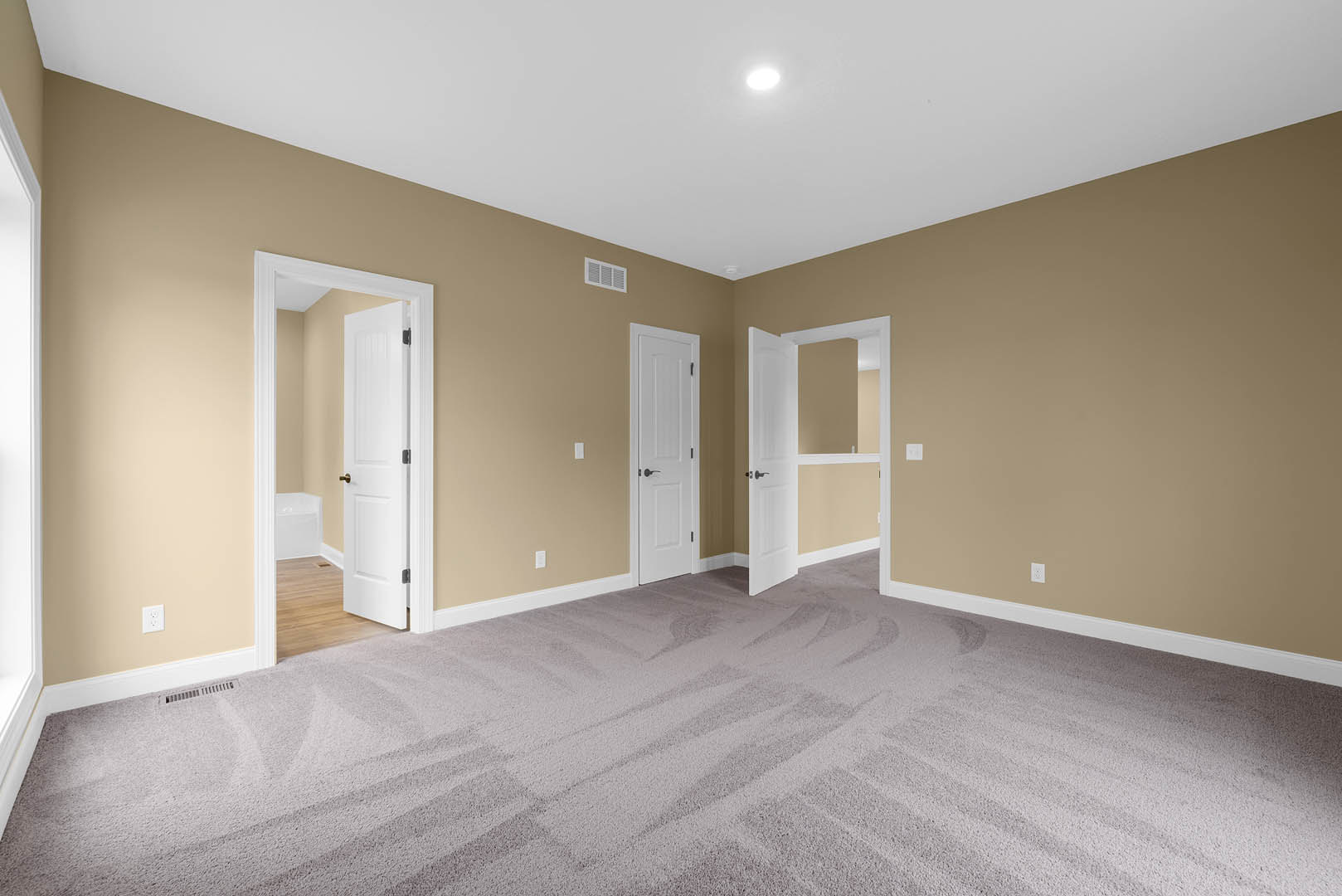 Beige walls with white trim, carpeted floor, three white doors featuring black, gold, and silver handles, plaster ceiling with bright overhead lighting