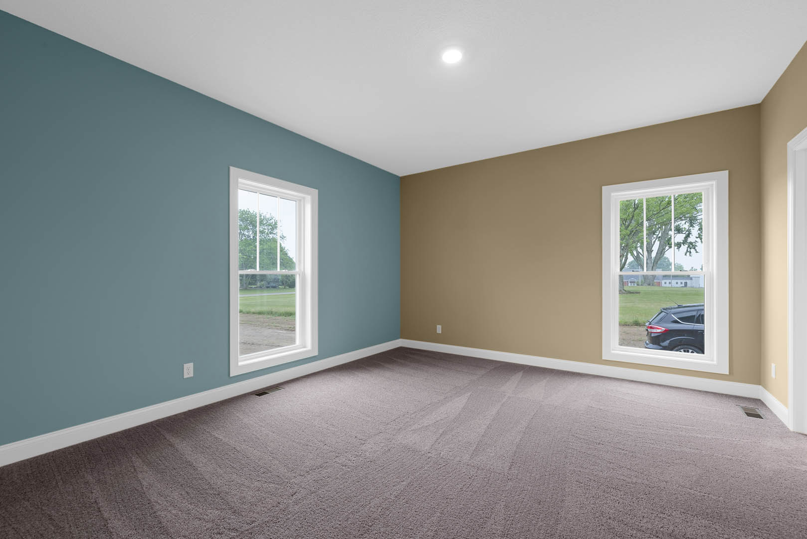 Carpeted room with white walls, large window overlooking green lawn and trees, natural light illuminating interior.