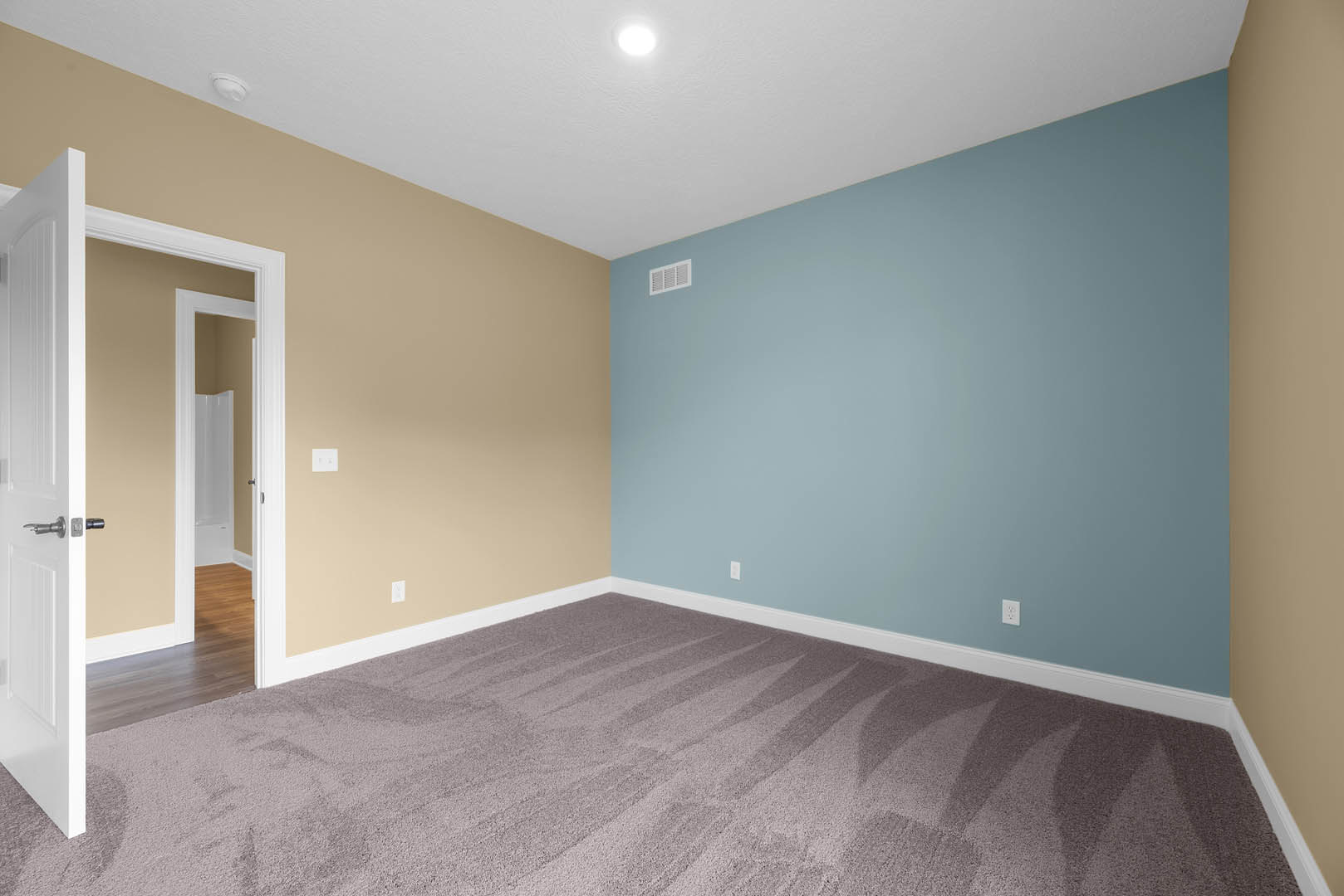 Blue accent wall and beige walls in a bright room with white ceiling, carpet flooring, door handle detail, wall vent, and decorative molding.