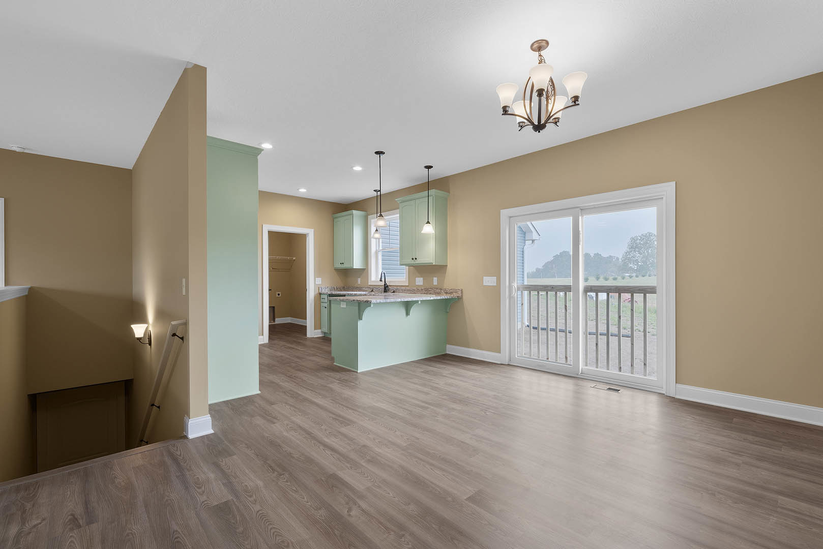 Open kitchen and dining area with wood flooring, white kitchen island featuring a sink, five-light pendant fixture above, sliding glass door with white frame, and adjacent white