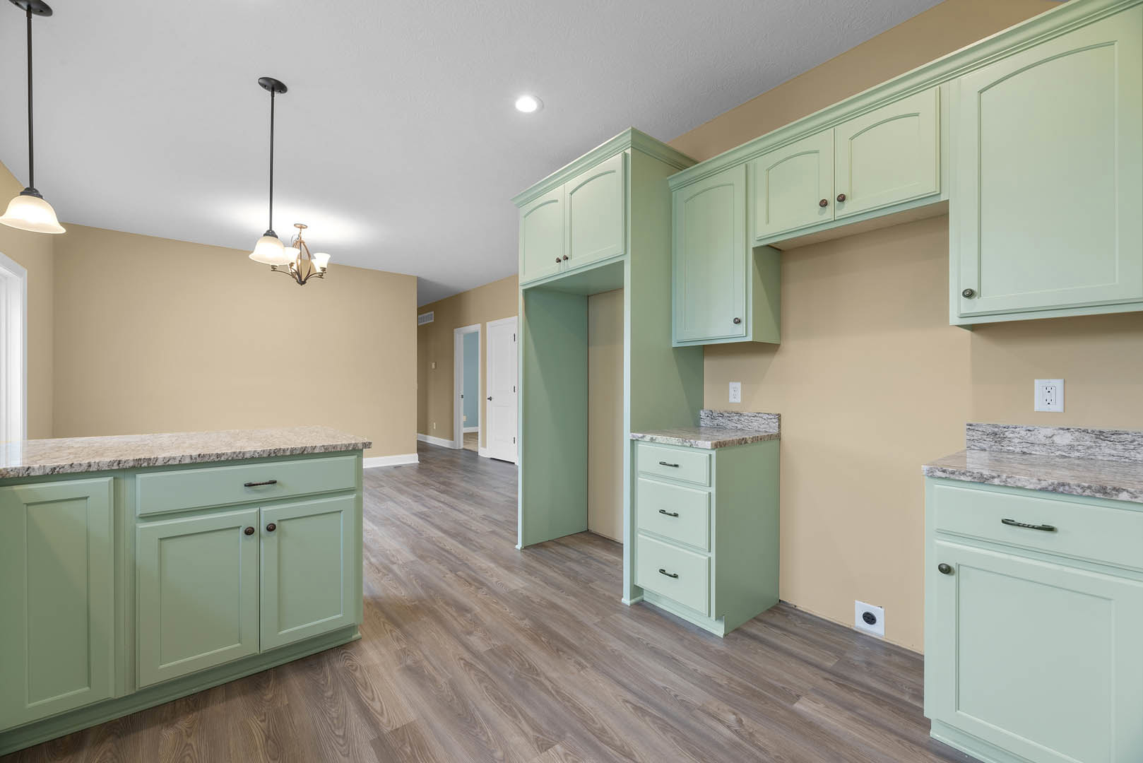 Green kitchen cabinets with marble countertop, wood flooring, white drawers, white electrical outlet on wall, close-up of white door and metal pole
