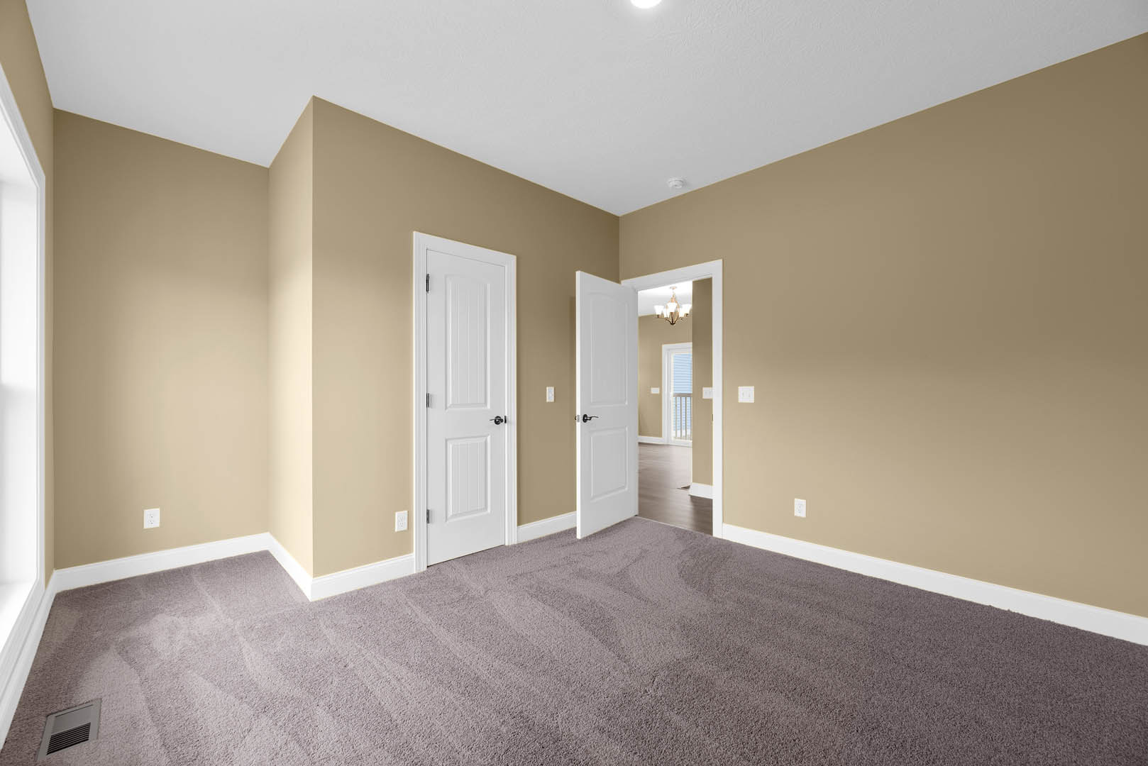 Beige-walled room with white doors featuring black handles, carpeted floor, wall vent, white ceiling with recessed light, and simple molding trim