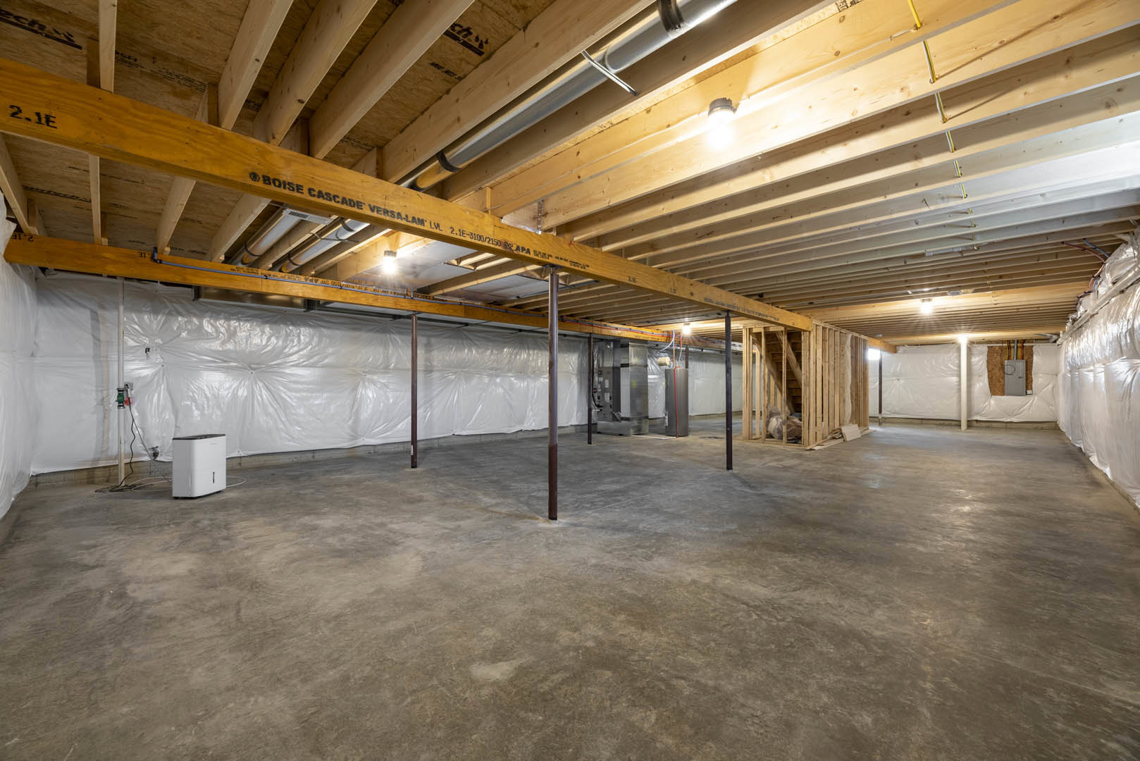 Spacious room featuring exposed wooden ceiling beams, smooth white plaster ceiling, concrete floor, and structural metal poles.