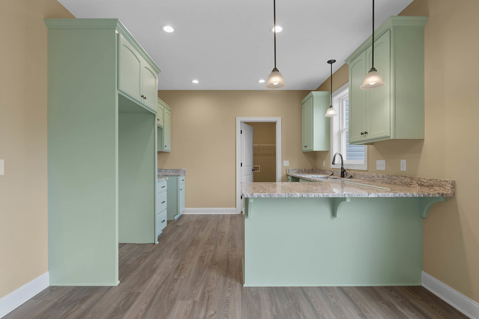 Marble kitchen countertop with wood flooring, light green wall, white cabinetry, and modern light fixture