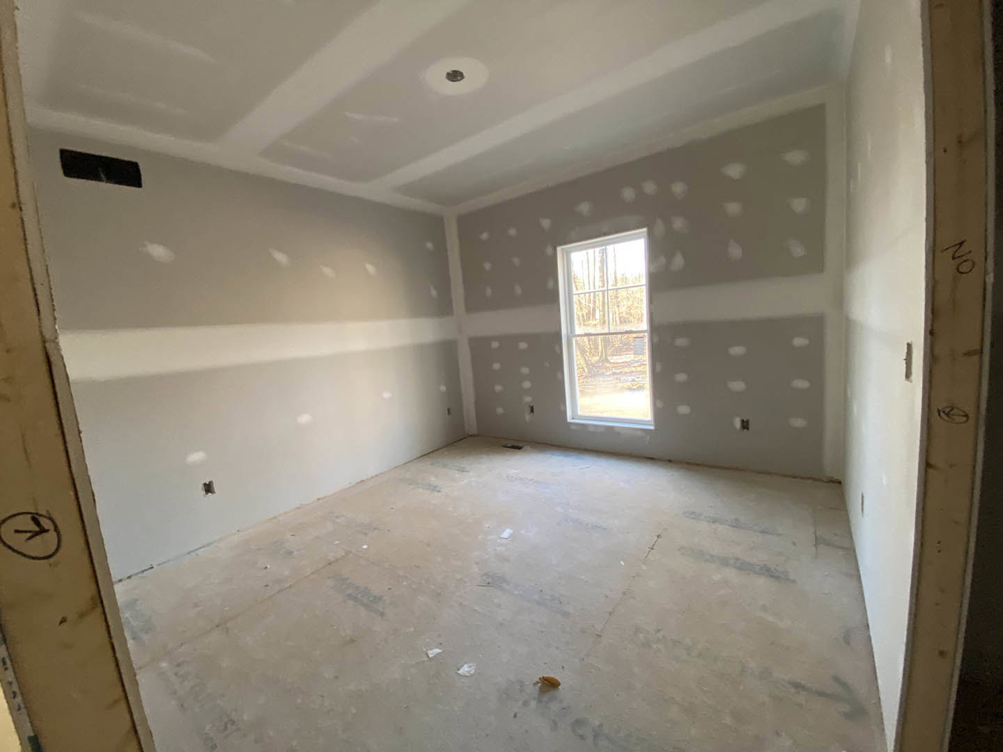Bright room with white plaster walls, two large windows showing green trees outside, light wood flooring, black wall clock with bird motif, and modern sink with circular drain.