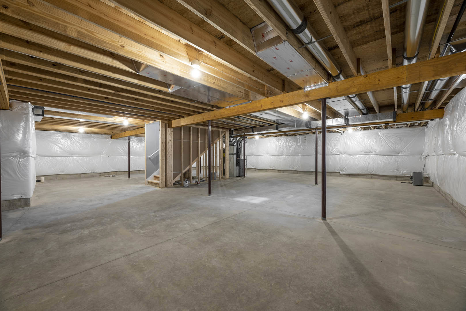 Open living space with exposed wooden ceiling beams, concrete floor, recessed ceiling light, and partial view of white tufted leather furniture.